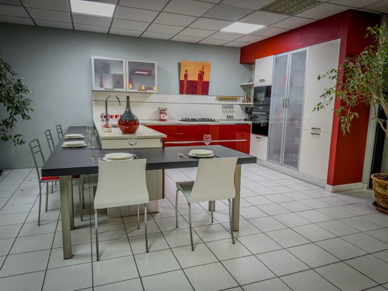 Vue d’ensemble d’une cuisine italienne sur mesure System Omicron exposée à Tresses, près de Bordeaux, associant laque brillante rouge et blanche, quartz Technistone et espace repas intégré.