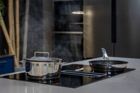 Cuisine italienne sur mesure alliant performance et design, avec plaque de cuisson aspirante 83 cm intégrée à un îlot central en quartz, showroom DB Design Cuisines à Tresses.